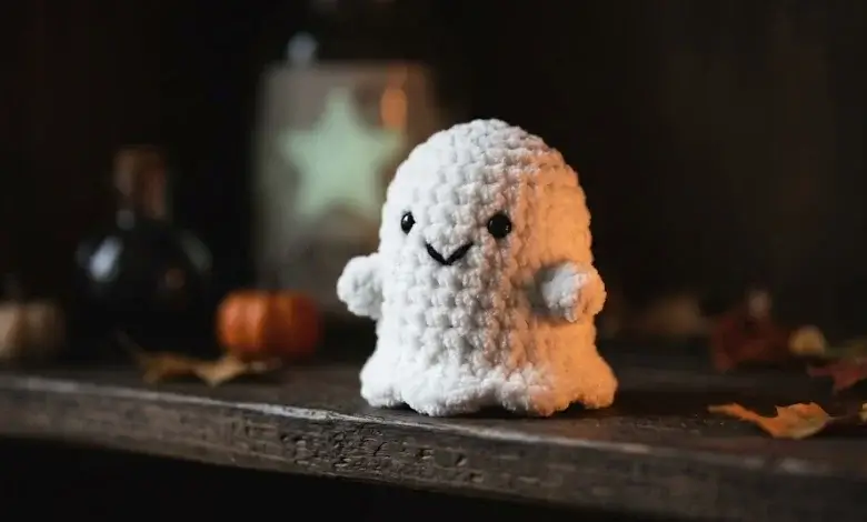 White chenille yarn crocheted ghost amigurumi on a dark wooden shelf with Halloween decor