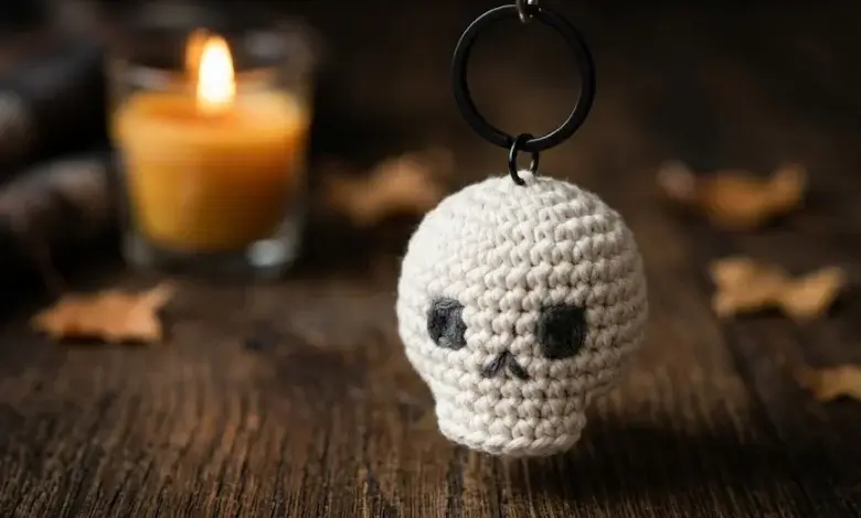 Small white crocheted skull keychain hanging from a black key ring against dark wood background
