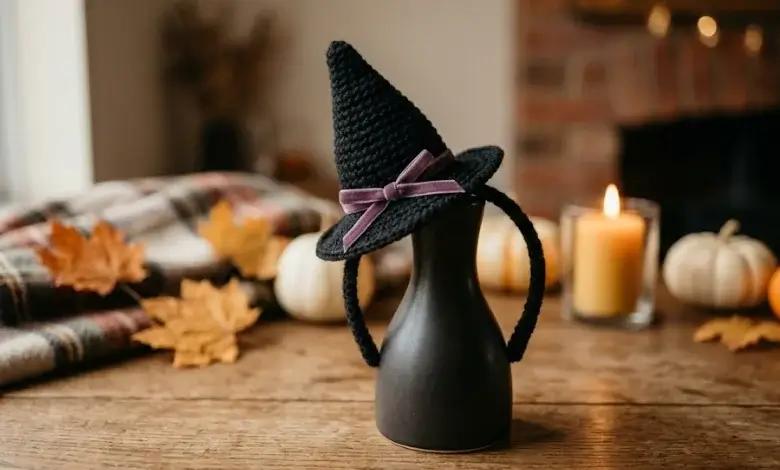 Black crocheted witch hat headband with purple ribbon displayed on a dark ceramic vase