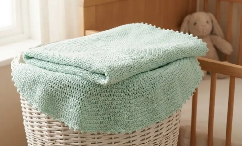 Soft mint green circular baby crochet blanket with picot edging folded in a white wicker basket