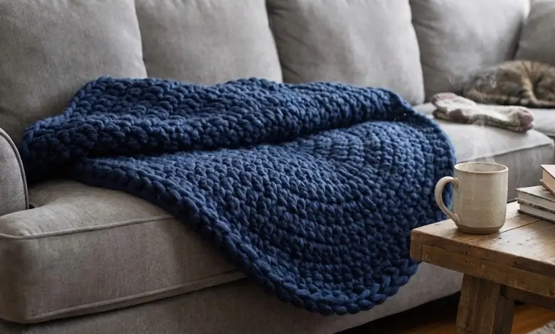 Thick chunky circular crochet blanket in deep navy blue super bulky yarn on a gray sofa with steaming mug