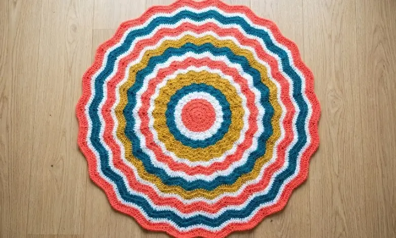 Circular crochet blanket with concentric ripple wave rings in coral white mustard and teal photographed from above