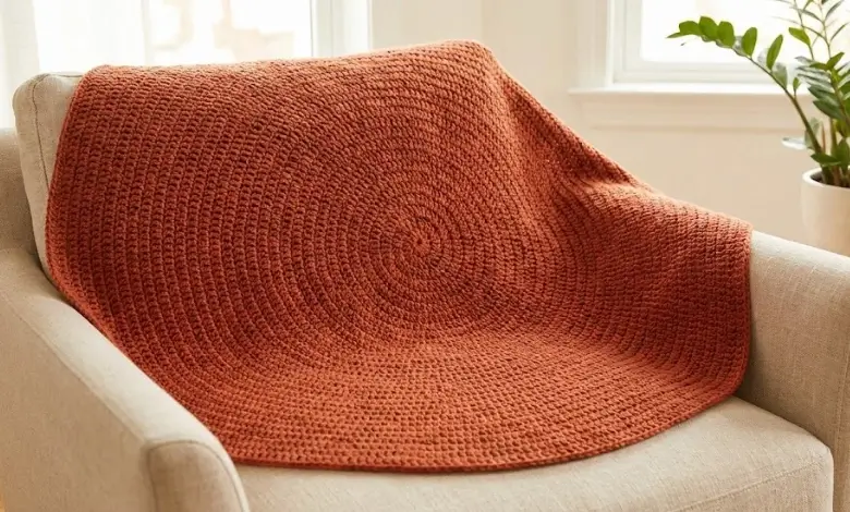 Free circular crochet blanket pattern in double crochet stitch draped over a neutral armchai