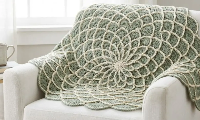 Sage green and cream circular crochet blanket with overlapping shell stitch petal pattern draped over a white armchair