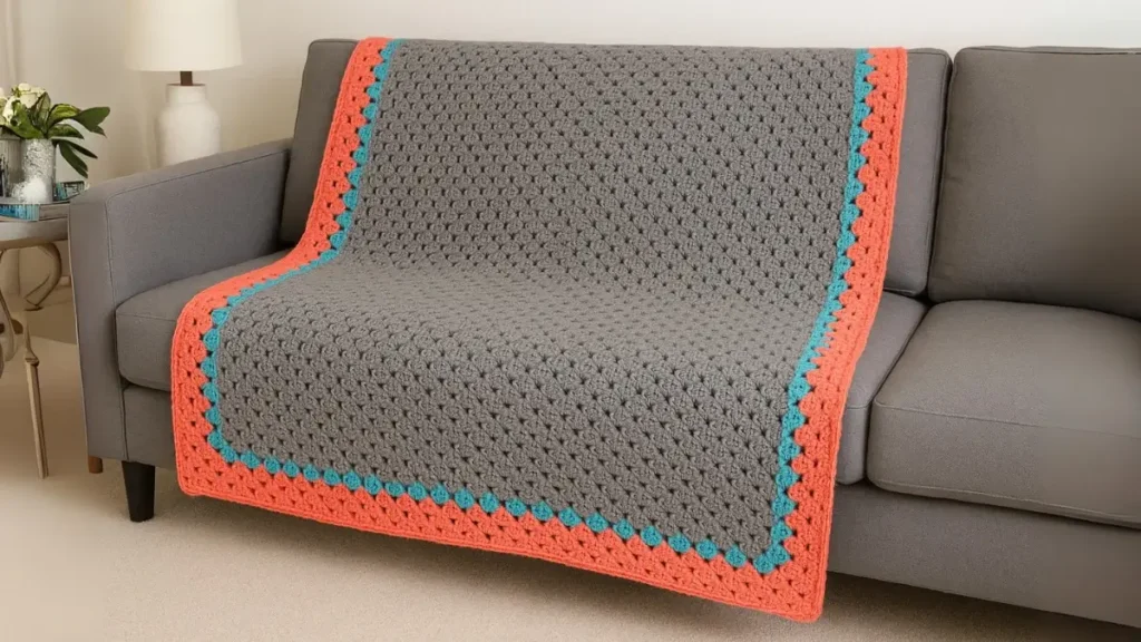 Modern giant granny square with gray center and vibrant coral-turquoise border on contemporary sofa