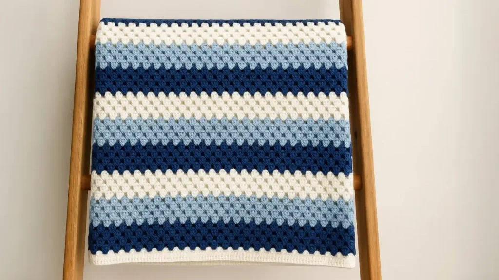 Horizontal stripe granny square afghan in navy, light blue, and white displayed on wooden ladder