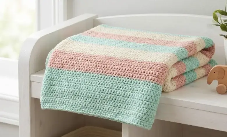 Soft baby crochet blanket with pastel mint green blush pink and cream horizontal stripes folded on a white nursery shelf