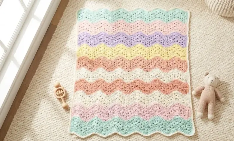 Cheerful baby crochet blanket combining granny stitch clusters and ripple waves in six pastel colors on a cream nursery rug