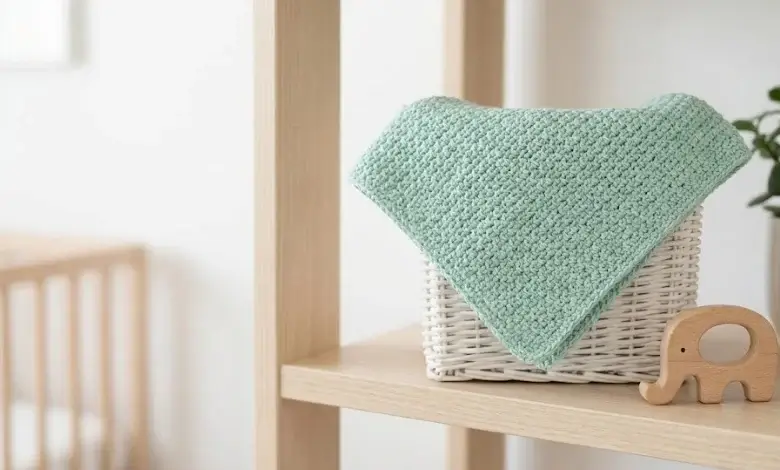 Soft mint green baby crochet blanket in moss stitch linen texture folded in a white wicker basket with wooden toy
