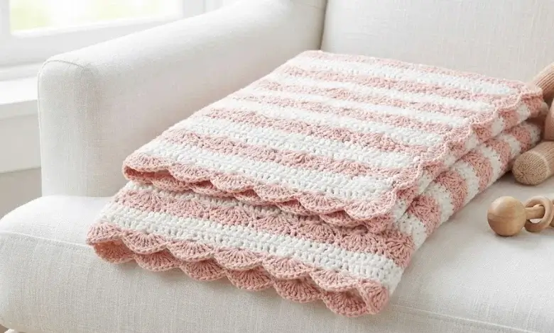White and blush pink baby crochet blanket with classic shell stitch scalloped texture folded on a white armchair