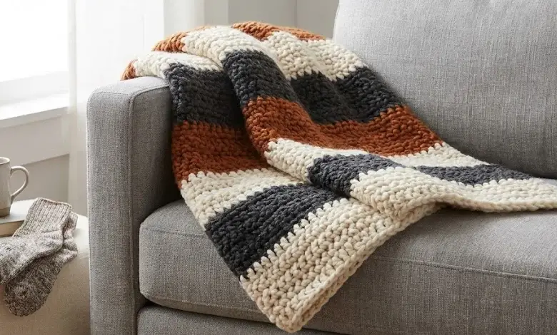 Thick bulky yarn crochet striped throw blanket folded on a gray sofa in a cozy home setting