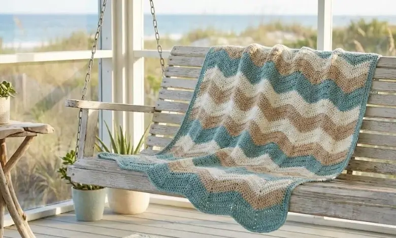 Soft blue and sandy beige crochet chevron throw blanket on a whitewashed porch swing by the ocean