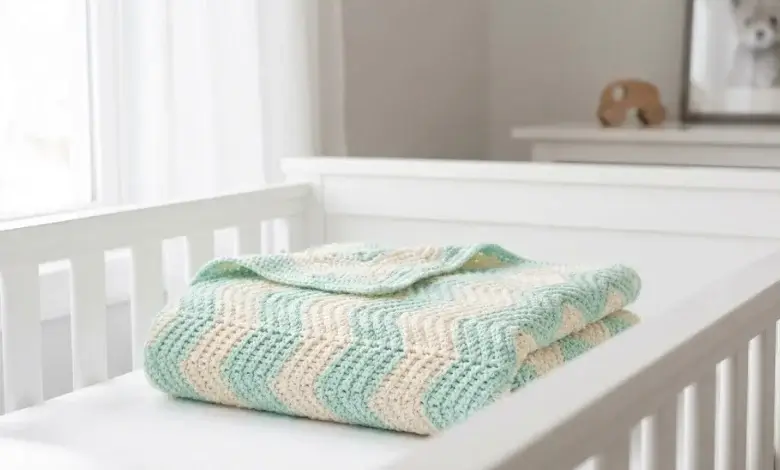Soft pastel mint and cream crochet chevron baby blanket folded in a white wooden crib