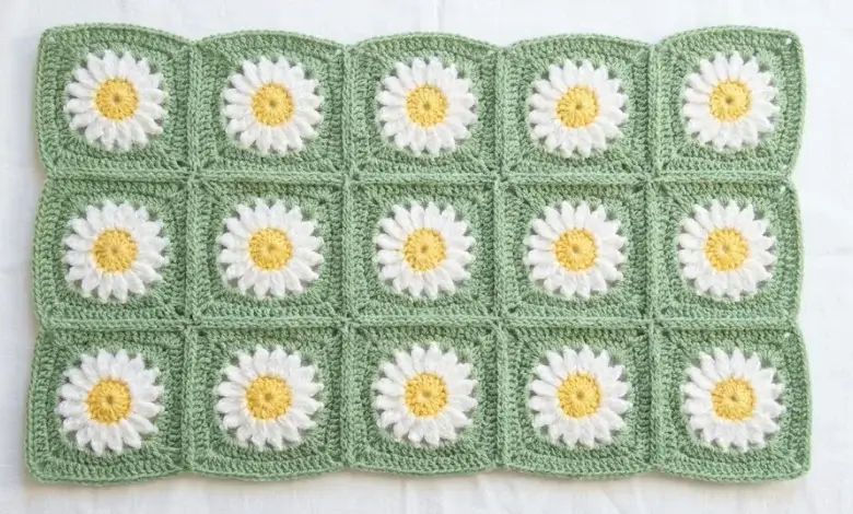 Crochet granny square baby blanket with yellow daisy motifs on soft green background laid flat