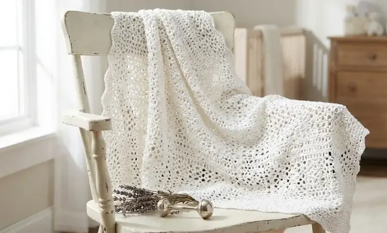 Delicate white lace crochet baby blanket draped over a vintage white wooden chair by a window