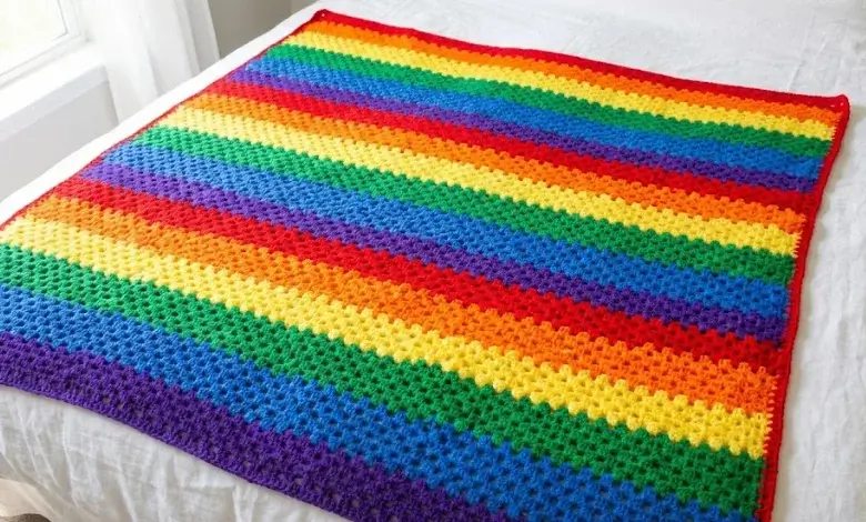 Colorful rainbow granny stitch crochet blanket with bold horizontal stripes laid flat on a white bed