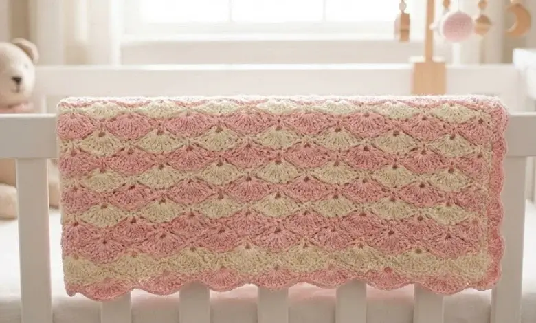 Soft pink and cream crochet shell stitch baby blanket folded in a white wooden crib