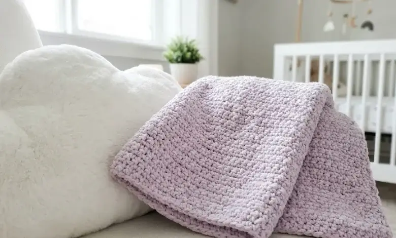 Pale lavender crochet moss stitch baby blanket folded on a cloud-shaped pillow in a modern white nursery