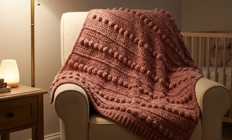Dusty rose velvet crochet baby blanket with raised bobble stitch texture draped over cream nursing chair